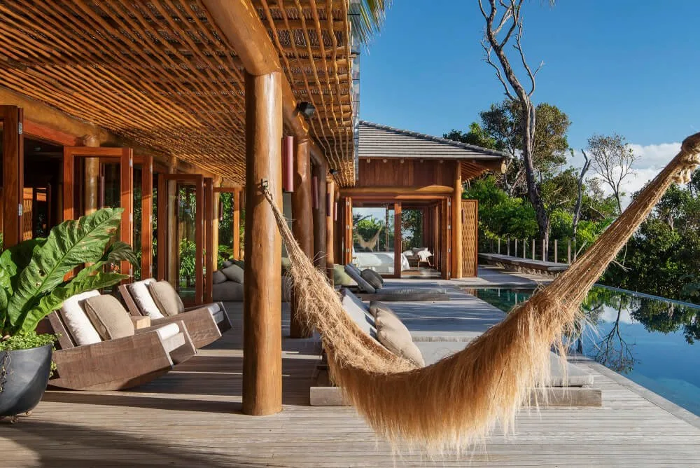 Covered timber terrace beside a pool with lounge seating, a hammock and open circulation