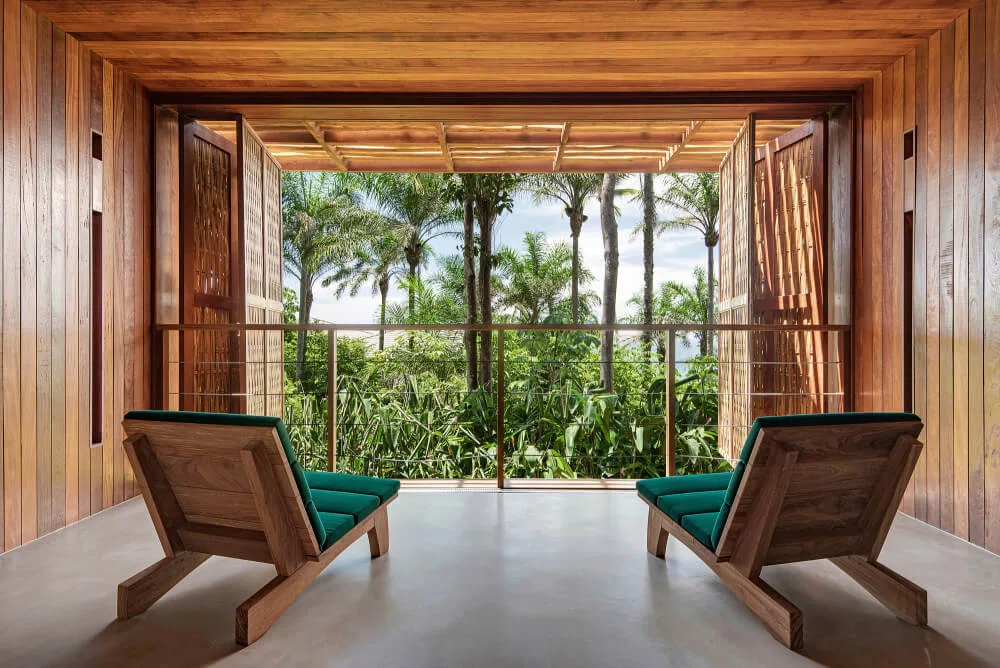 Two timber lounge chairs on a covered veranda looking toward palms and the sea