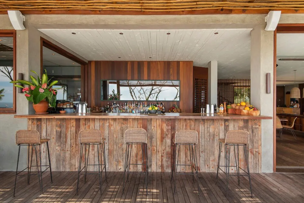 Timber-fronted resort bar counter with five high stools beneath a covered roof