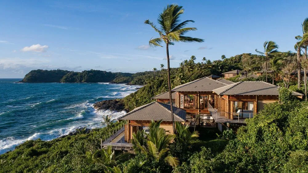 Coastal resort buildings set among palms and dense planting above the sea